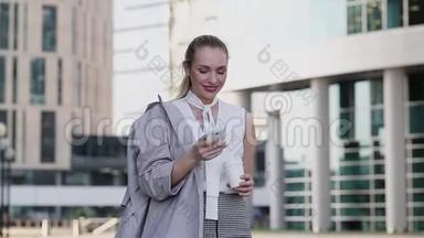 一位年轻的女商人站在市中心，用智能<strong>手机端</strong>着一杯咖啡